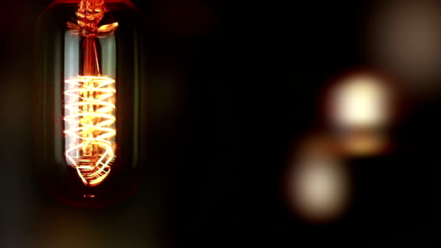 turn-on-and-turn-off-in-slow-motion,-retro-vintage-light-bulb-with-old-technology-with-filament-built-in-with-warm-light-yellow-tint-and-black-background-with-unfocused-retro-bulbs,-vintage-object-old-style