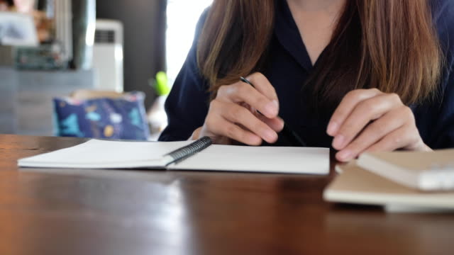 Closeup-imagen-de-una-mujer-abriendo-un-cuaderno-en-blanco-para-escribir-en-la-mesa-de-madera
