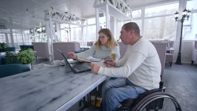 erfolgreiche-ungültig-Mann-Restaurantbesitzer-am-Rollstuhl-mit-Frau-arbeitet-auf-Laptop-Computer-für-die-Planung-und-Verwaltung-von-Unternehmen-und-Ideen-zu-entwickeln