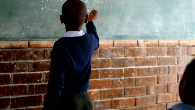 Schoolboy-writing-on-chalkboard-in-classroom-4k