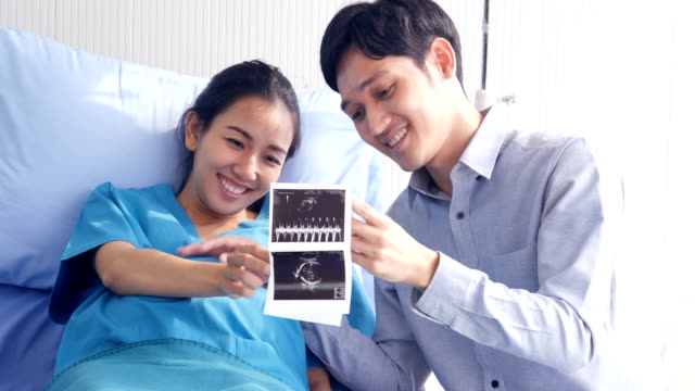 Schwangere-Frau-und-Mann-auf-der-Suche-nach-Röntgen-Film-mit-glücklichen-Emotionen-zusammen.-Menschen-mit-Gesundheits--und-medizinischen-Konzept.
