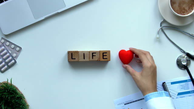 Life-word-composed-of-wooden-cubes-by-female-doctor-hand,-toy-heart-lying-near