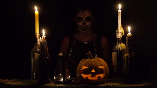 Halloween-witch-licks-knife-blade-in-chains-with-skull-makeup-magic-pumpkin-and-candles