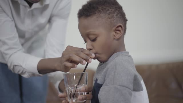 Betreuende-Mutter-hilft-kleinen-afrikanischen-Amerikanischen-Jungen,-Wasser-zu-trinken