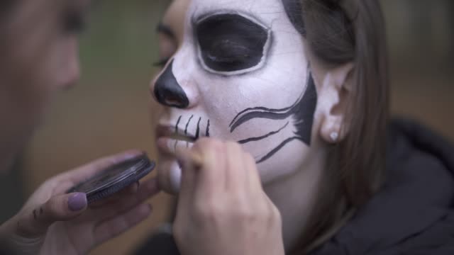 Nahaufnahme-eines-kaukasischen-Mädchens,-das-Halloween-Make-up-auf-dem-Gesicht-ihres-Freundes-malt.