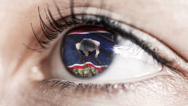 Woman-green-eye-in-close-up-with-the-flag-of-Wyoming-state-in-iris,-united-states-of-america-with-wind-motion.-video-concept