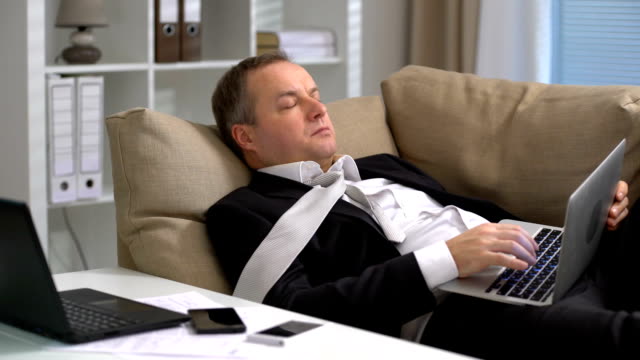 Müde-Geschäftsmann-arbeitet-mit-Laptop-und-schläft-auf-dem-Sofa-im-Büro