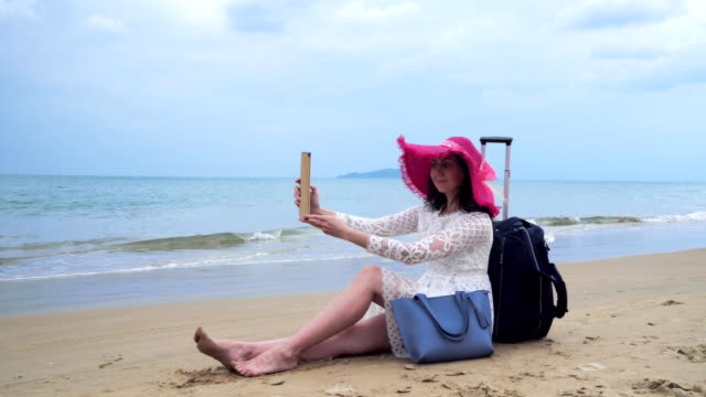 Girl-seats-on-the-beach-with-her-bagage-and-tablet-computer