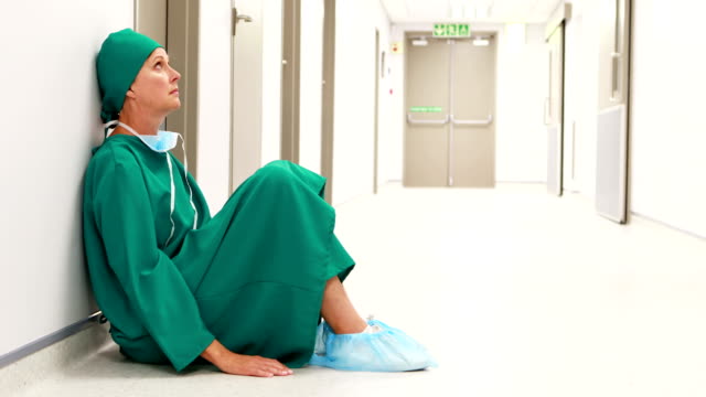 Tensed-female-surgeon-sitting-in-corridor