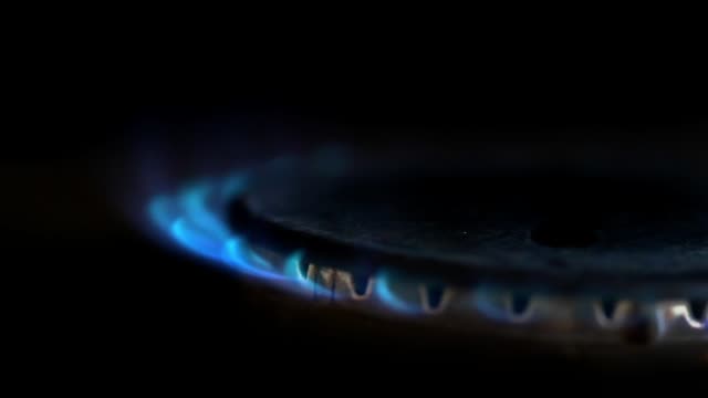 Close-up-of-gas-stove-blue-flame-lit-in-a-dark-kitchen
