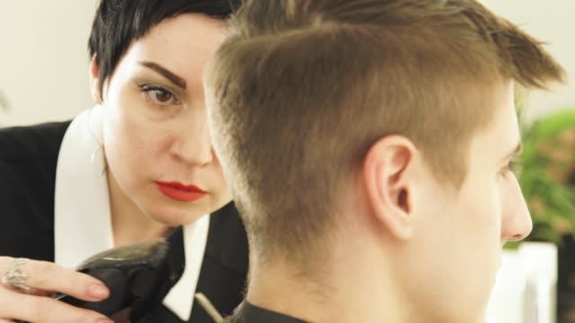 Hairdresser-cutting-male-hair-with-electric-shaver-in-beauty-school.-Woman-haircutter-making-male-haircut-with-hair-clipper-in-barbershop-close-up