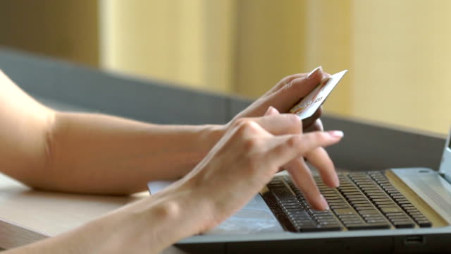 Primer-plano-de-la-mujer-de-las-manos-manteniendo-una-tarjeta-de-crédito-y-usando-el-teclado-de-la-computadora-para-compras-en-línea