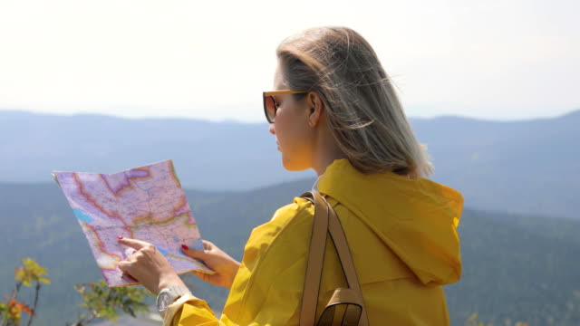 Hiker-in-a-yellow-raincoat-looking-at-map-from-mountain-top.-woman-with-map-in-mountains-FullHD