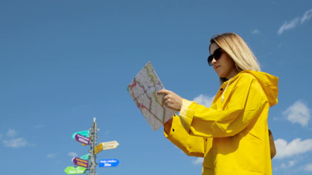Junge-Frau-Im-gelben-Regenmantel-mit-einem-Rucksack-in-Bergen-Papierkarte-in-Händen-hält,-Wandern