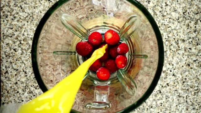 Orange-juice-flows-in-a-blender-bowl-on-strawberry.-Slow-motion.	Shooting-in-kitchen.-Top-view.