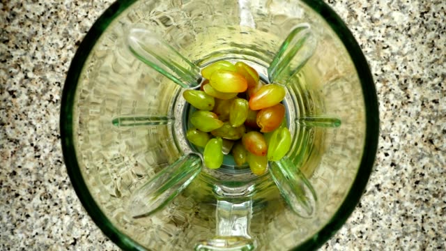 Pieces-of-apples-fall-in-a-blender-bowl-on-grapes.-Slow-motion.	Shooting-in-kitchen.-Top-view.