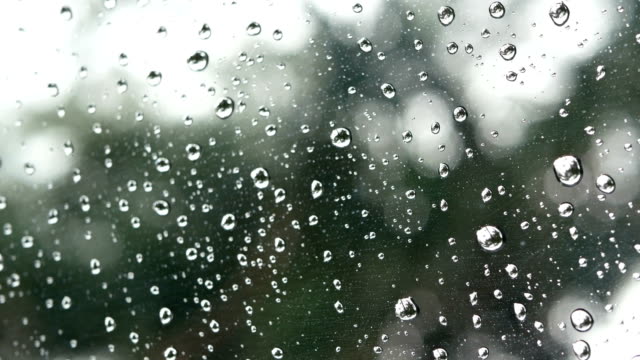 4K-Filmmaterial.-Regen-auf-Sichtfenster-Glasoberfläche-mit-grüner-Baum-und-Bokeh-Licht-außerhalb-im-Hintergrund-läuft.-Regentropfen-in-regnerischen-Tag