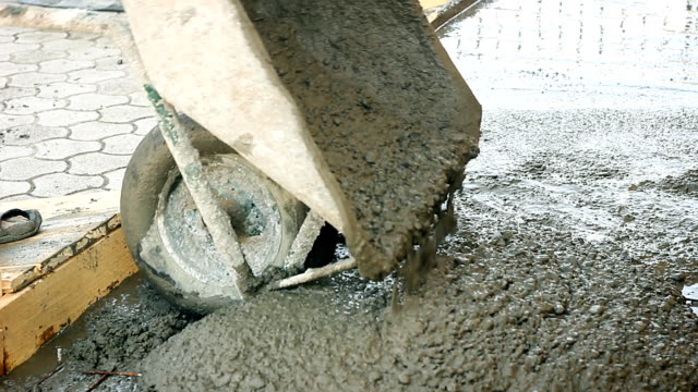 Construction-worker-pushing-wheelbarrow-with-liquid-concrete-on-building-site