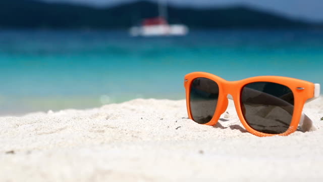 Gafas-de-sol-moda-naranja-brillantes-en-la-blanca-arena-de-una-playa-tropical