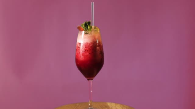Der-Cocktail-dreht-sich-auf-einem-farbigen-Hintergrund,-der-Cocktail-dreht-sich-um-die-eigene-Achse,-der-Cocktail-mit-Eis,-verziert-mit-Minze