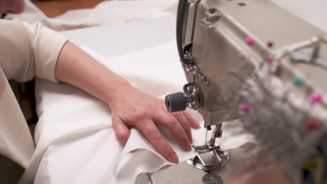 A-closeup-top-view-of-woman's-hands-stitching-white-fabric-on-the-sewing-machine.-The-process-of-sewing-a-wedding-dress