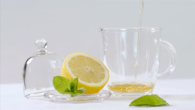 Kräutertee-in-transparenten-Teekanne,-Zitrone-und-Minze-Blätter-herum,-75-fps-Slow-motion