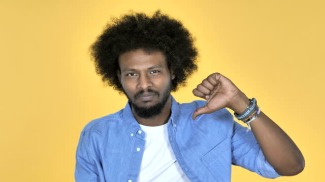 Afro-amerikanischer-Mann-gestikulieren-Daumen-nach-unten-auf-gelbem-Hintergrund