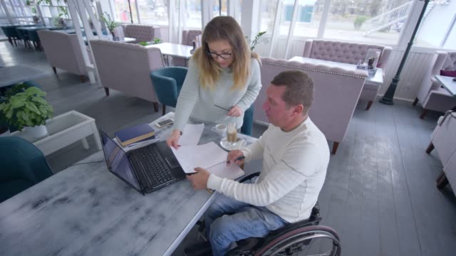 tutoring-for-disabled,-successful-crippled-man-in-wheelchair-with-educator-woman-using-smart-computer-technology-during-personal-lesson