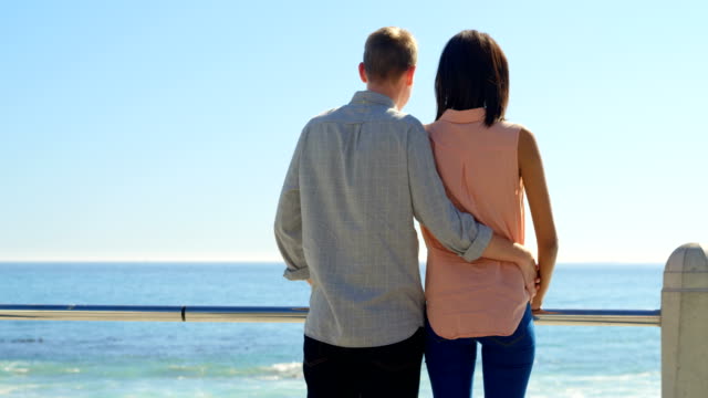 Rear-view-of-couple-talking-while-looking-at-the-calm-sea-4k