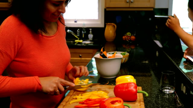 Kinder,-die-mit-Laptop-und-digital-Tablette-während-Mutter-schneiden-Gemüse-4k