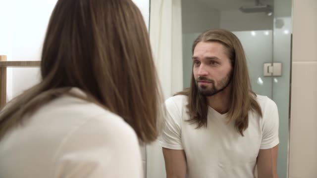 Man-At-Bathroom-Looking-In-Mirror-And-Touching-Face