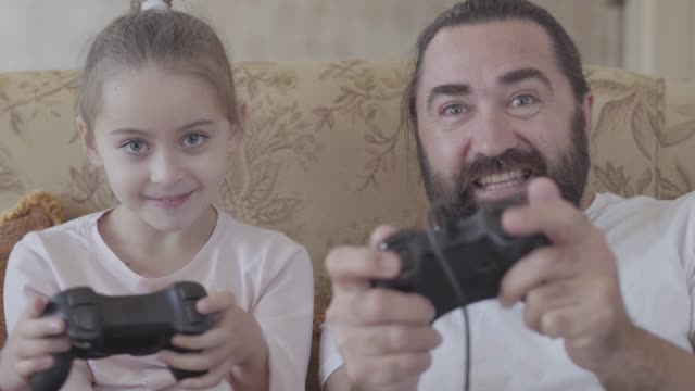 Kleine-Tochter-mit-ihrem-lustigen-Vater,-die-Videospiele-im-Fernsehen-mit-großen-Emotionen-im-gemütlichen-Wohnzimmer-spielt.