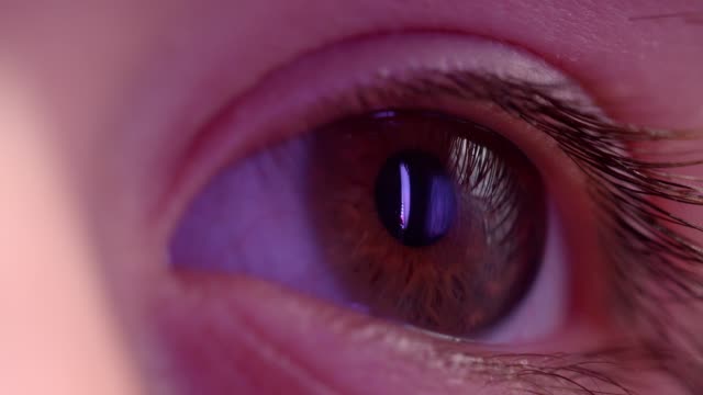 Close-up-shoot-of-l-eye-watching-rightwards-with-reflection-of-violet-lamp-in-it.