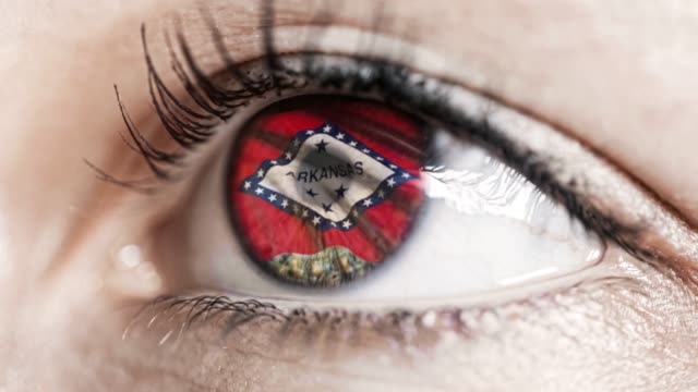 Mujer-ojo-verde-en-primer-plano-con-la-bandera-del-estado-de-Arkansas-en-iris,-estados-unidos-de-América-con-movimiento-de-viento.-concepto-de-vídeo