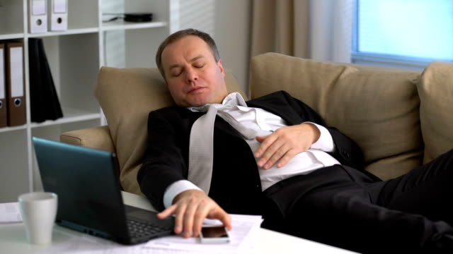 Müder-Geschäftsmann-schläft-auf-dem-Sofa-im-Büro