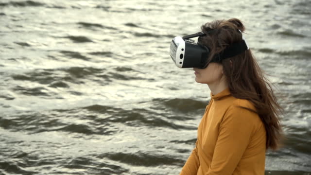 Una-mujer-joven-utiliza-gafas-de-realidad-virtual-junto-a-fuerte-oleaje.