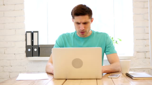 Young-Man-Working-on-Laptop-Reacting-to-Failure-and-Upset-by-Loss