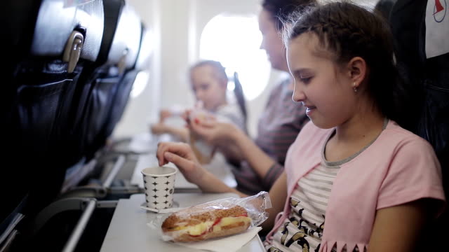Young-woman-sits-in-chair-near-illuminator-of-airplane-and-eats-meal-for-passenger