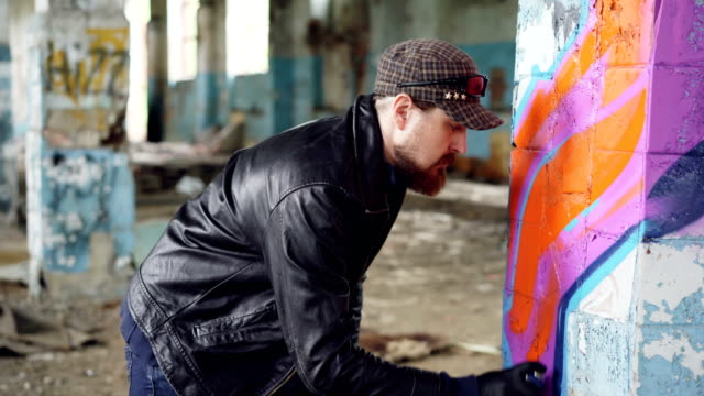 Handosme-Mann-Graffiti-Künstler-konzentriert-sich-auf-Lackierstraßen-mit-Aerosol-Farbe-auf-Spalte-in-alten-leeren-Haus.-Verlassene-Gebäude,-Wand-Kunst-und-Kreativität-Konzept.