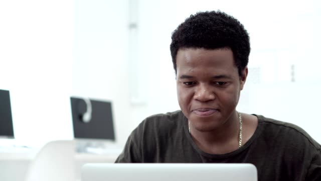 Close-up-of-African-American-student-smiling-while-reading-email-message-on-his-laptop-computer