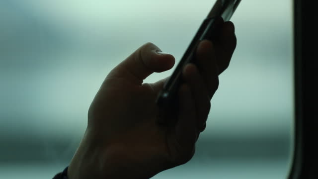 Close-up-of-person-holding-cellphone-device-while-on-a-moving-train.-Blurred-background-moving-in-motion