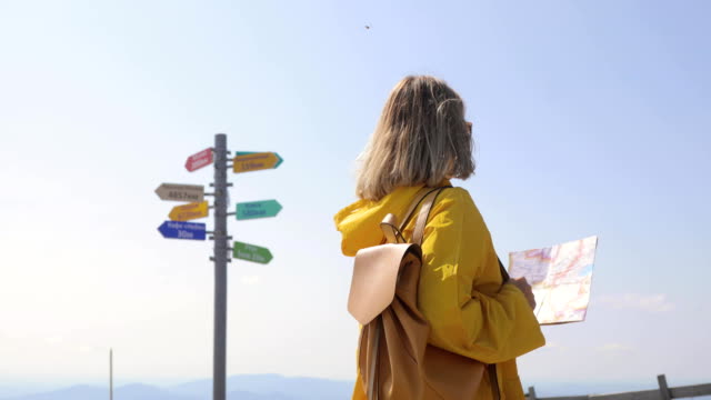 Rückansicht-des-kaukasischen-weibliche-Wanderer-im-gelben-Regenmantel-steht-in-den-Bergen-mit-einer-Karte-in-der-hand