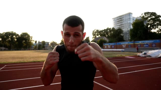 Handhelded-close-up-footage-of-an-angry-male-boxer-training-on-the-outdoors-stadium.-Portrait-of-a-man-boxing-with-invisible-opponent,-punching