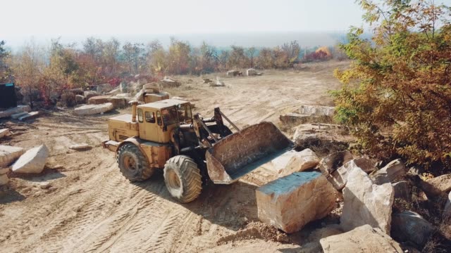 professional-yellow-bulldozer-with-a-bucket-is-working-in-the-quarry-with-stones-on-the-background-of-sand.