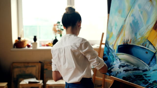 Pintor-profesional-femenino-trabaja-en-cuadro-con-óleo-y-espátula-creando-hermoso-paisaje-sobre-lienzo.-Concepto-de-técnica-y-herramientas-de-pintura.