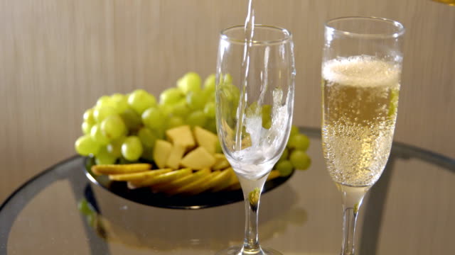 Cita-romántica.-Derramar-champán-en-copas-sobre-una-mesa-con-frutas