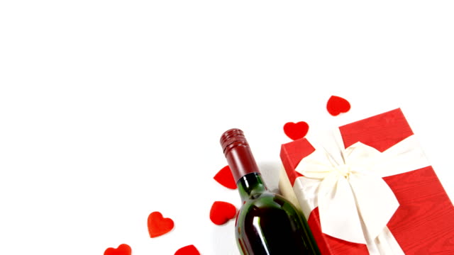 Botella-de-vino,-caja-de-regalo-y-dispersos-corazones-rojos-sobre-blanco-superficie-4k