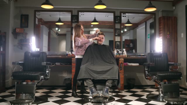 Innenaufnahme-des-Arbeitsprozesses-in-modernen-Friseursalon.-Seite-Ansicht-Porträt-der-attraktive-junge-Mann-immer-trendigen-Haarschnitt.-Männliche-Friseur-servieren-Kunden,-was-Haarschnitt-mit-Metall-Schere-und-Kamm