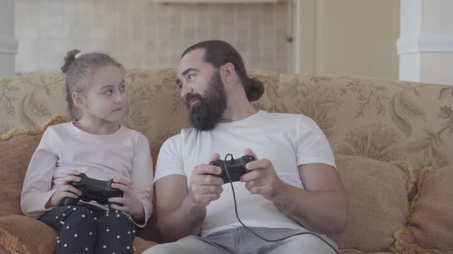 Small-daughter-with-her-funny-father-playing-video-games-on-tv-with-great-emotions-in-cozy-living-room.
