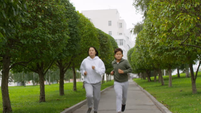 Madre-asiática-e-hijo-corriendo-a-lo-largo-de-Green-Alley-con-árboles